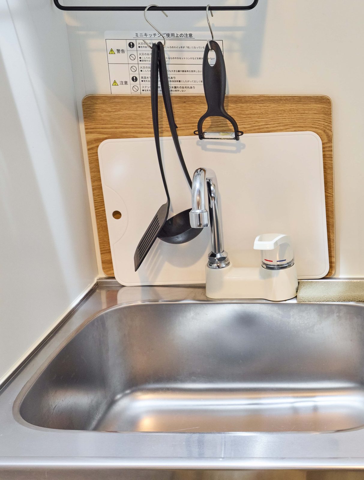 心斎ノ翼 C 房型廚房的不鏽鋼水槽與流理台，後方立著砧板、牆上掛著鍋鏟